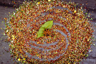Spices arranged in a circular pattern with a star anise and leaf on a dark surface