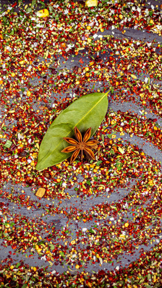 Spices arranged in a circular pattern with a star anise and leaf on a dark surface