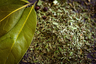 A bay leaf sitting on a spice pile of various green herbs.